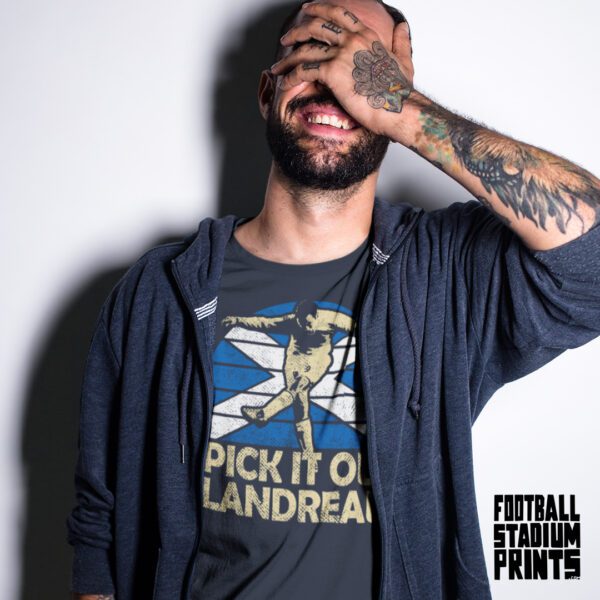 A man smiling with one of his hands on his face wearing a navy t-shirt featuring James McFadden and the slogan, "Pick it out, Landreau!"