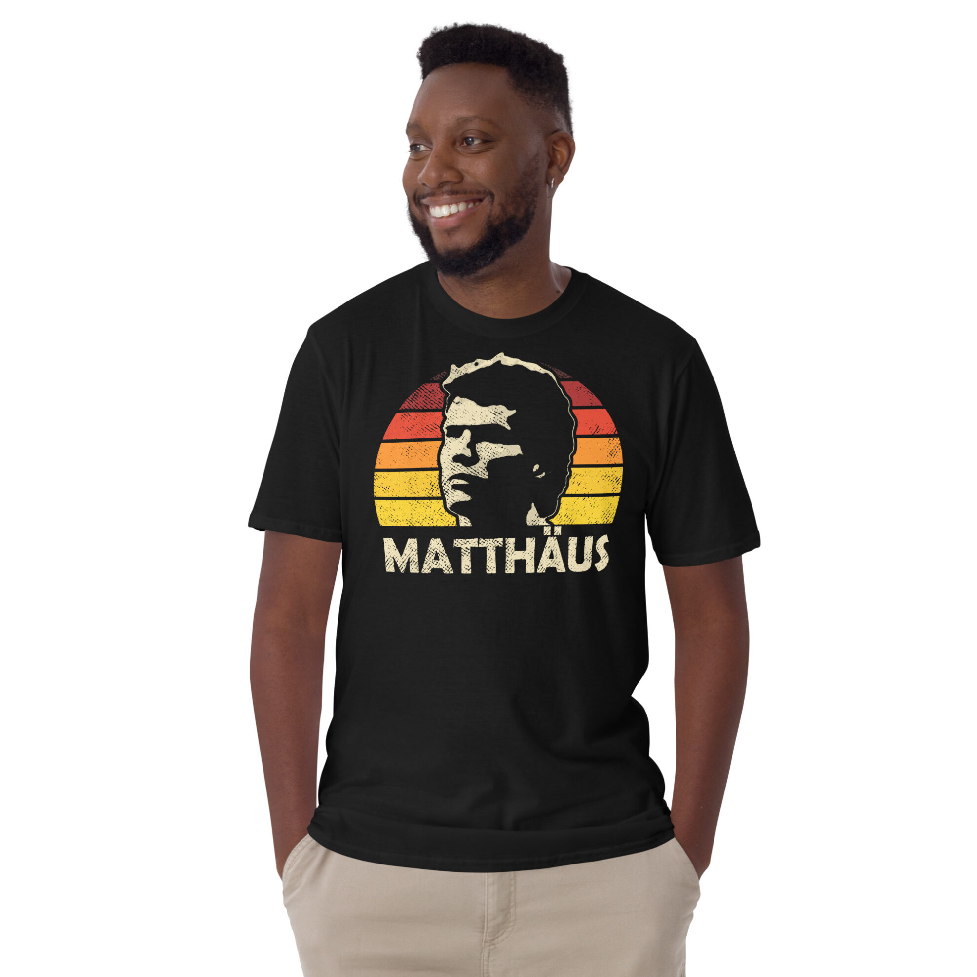 A man wearing a Lothar Matthäus T-Shirt in Black: A black T-shirt featuring a black, red, and gold sunburst and the word "MATTHÄUS" in bold, honoring German football legend Lothar Matthäus.