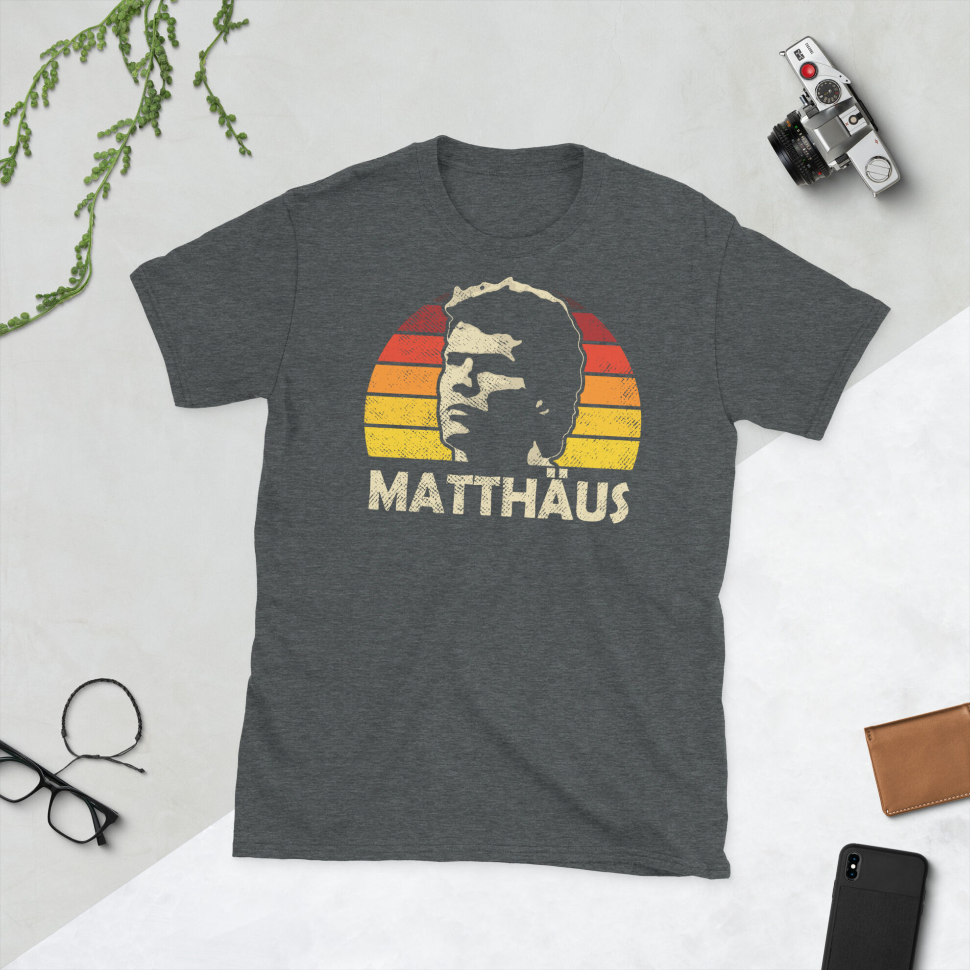Lothar Matthäus T-Shirt in Heather: A heather grey T-shirt featuring a black, red, and gold sunburst and the word "MATTHÄUS" in bold, commemorating German football legend Lothar Matthäus.