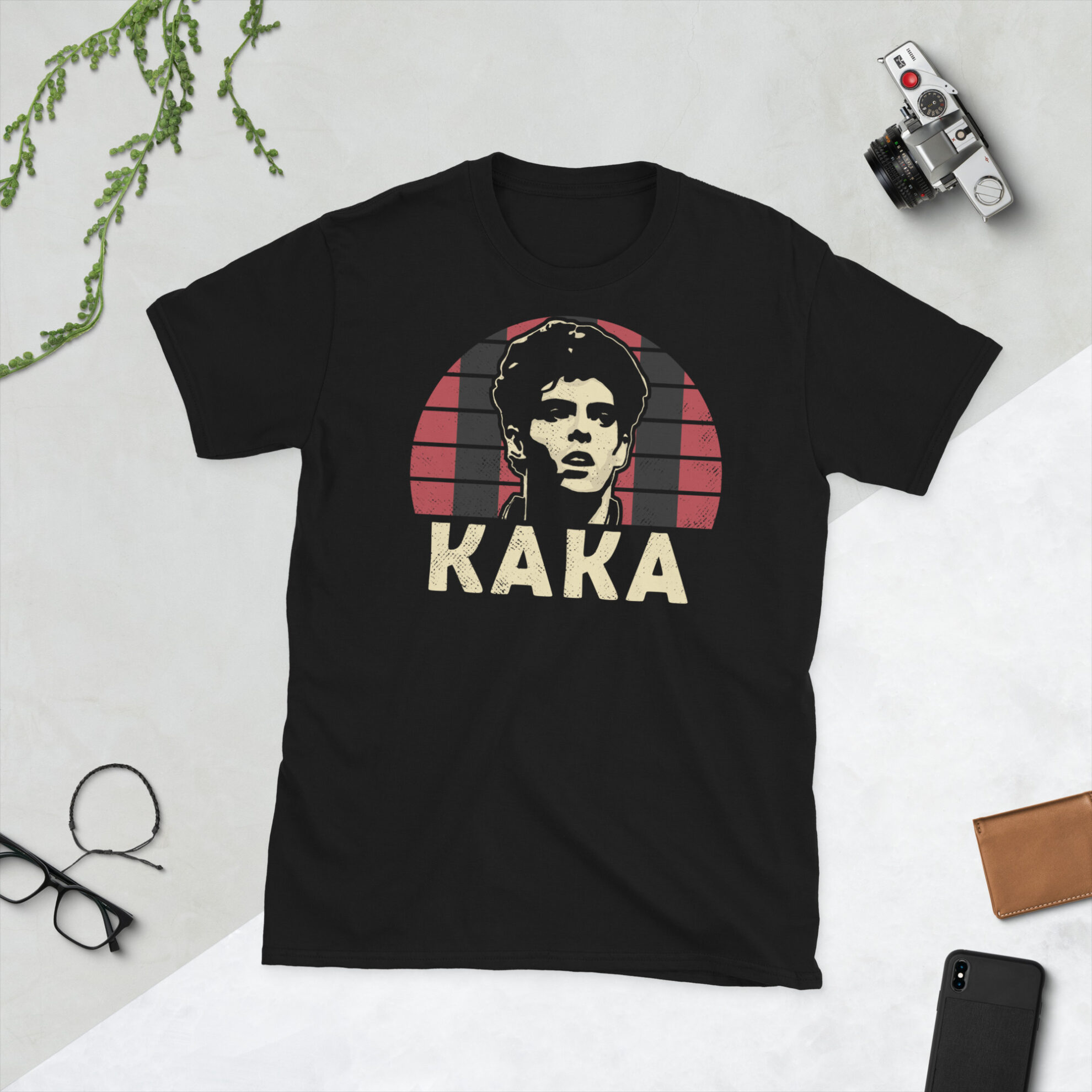 A black Kaka T-Shirt featuring a red and black striped sunburst design (inspired by AC Milan colours) and "KAKA" printed prominently in bold.