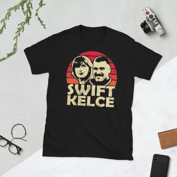 A black Taylor Swift & Travis Kelce T-shirt featuring silhouettes of Swift and Kelce and a red and yellow sunburst.