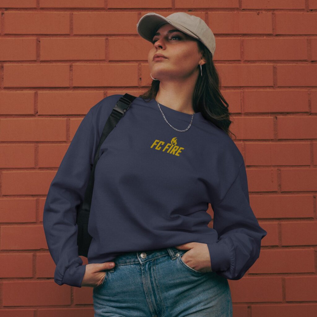 A young woman wearing FC Fire’s navy blue premium embroidered long-sleeve sweater – luxury football streetwear from Enfield, UK