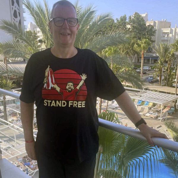 A smiling man wearing an Aberdeen Scottish Cup winning t-shirt featuring Graeme Shinnie lifting the cup and the slogan Stand Free