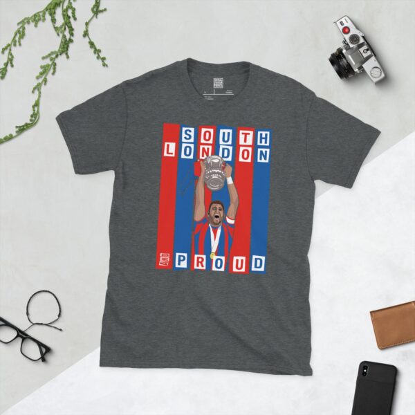 A dark heather T-shirt featuring a graphic of Crystal Palace legend Joel Ward lifting the FA Cup, set against bold blue and red stripes. The text "SOUTH LONDON" is at the top and "AND PROUD" is at the bottom.