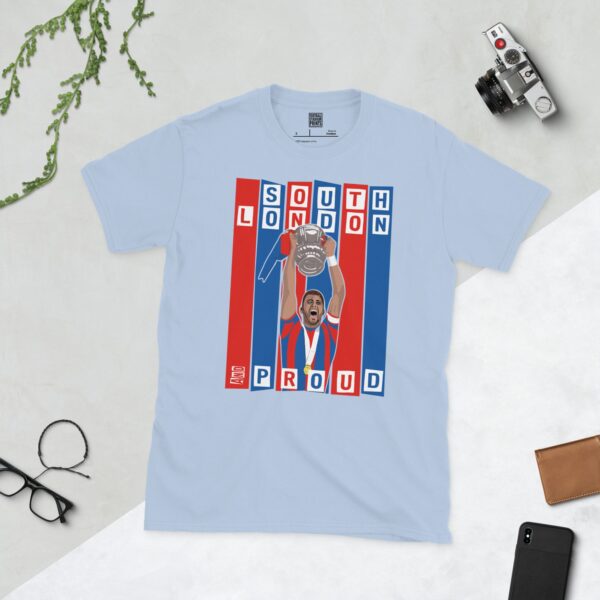 A baby blue T-shirt featuring a graphic of Crystal Palace legend Joel Ward lifting the FA Cup, set against bold blue and red stripes. The text "SOUTH LONDON" is at the top and "AND PROUD" is at the bottom.