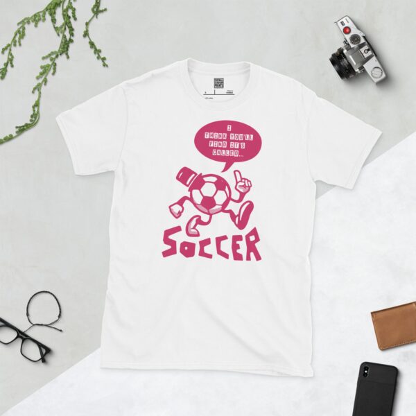A white T-shirt featuring a pink cartoon football character with a top hat, arms, and legs, pointing. A speech bubble above reads "I THINK YOU'LL FIND IT'S CALLED..." and "SOCCER" is written below the character.