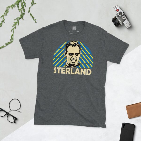 A subtle dark heather T-shirt displaying a distinctive graphic of former Leeds United player Mel Sterland. Behind him, a sunburst design in characteristic blue and yellow patterns radiates, and his name "STERLAND" is displayed at the bottom of the graphic.