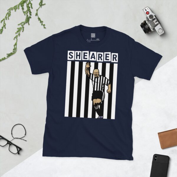 A versatile Navy T-shirt featuring a striking illustration of Alan Shearer, the revered Newcastle United striker, in his traditional black and white kit with his arm raised in triumph. His surname "SHEARER" is positioned above the graphic, completing the tribute.