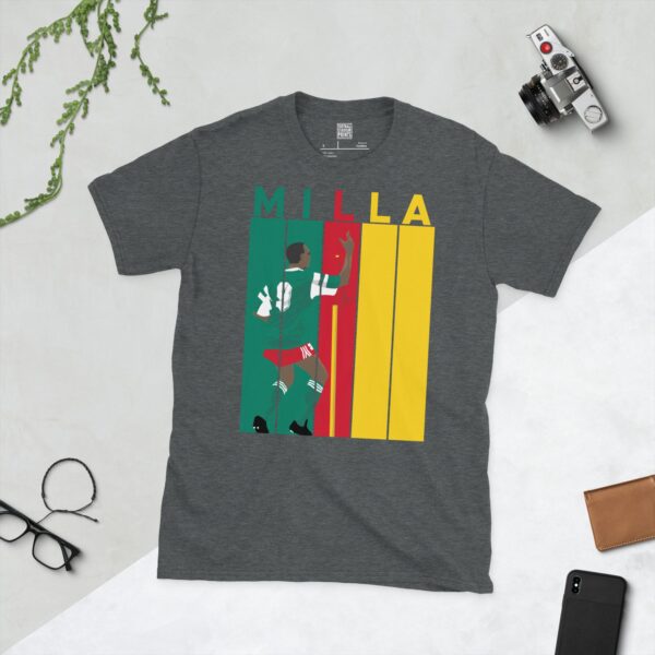 A dark heather Roger Milla T-shirt featuring a bold striped design in Cameroon flag colours, with "MILLA" above five pillars and a graphic of Roger Milla doing his iconic corner flag dance from the 1990 World Cup.