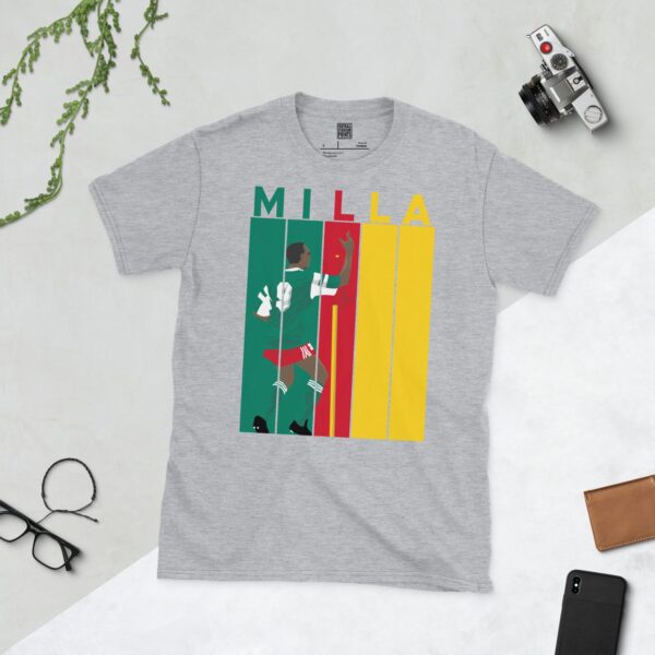 A sports grey Roger Milla T-shirt featuring a bold striped design in Cameroon flag colours, with "MILLA" above five pillars and a graphic of Roger Milla doing his iconic corner flag dance from the 1990 World Cup.