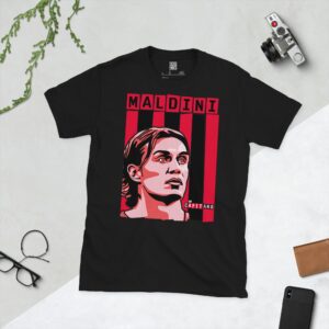 A bold black T-shirt displaying a vivid illustration of AC Milan icon Paolo Maldini's face. Behind him are classic red and black vertical stripes, evoking the iconic Rossoneri kit. His surname "MALDINI" and the famous title "IL CAPITANO" are prominently featured in block letters.