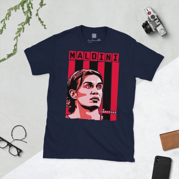 A deep navy blue T-shirt featuring a compelling graphic of Paolo Maldini, the legendary AC Milan captain, set against a backdrop of bold red and black vertical stripes. His surname "MALDINI" and the iconic phrase "IL CAPITANO" are clearly visible, celebrating his status.