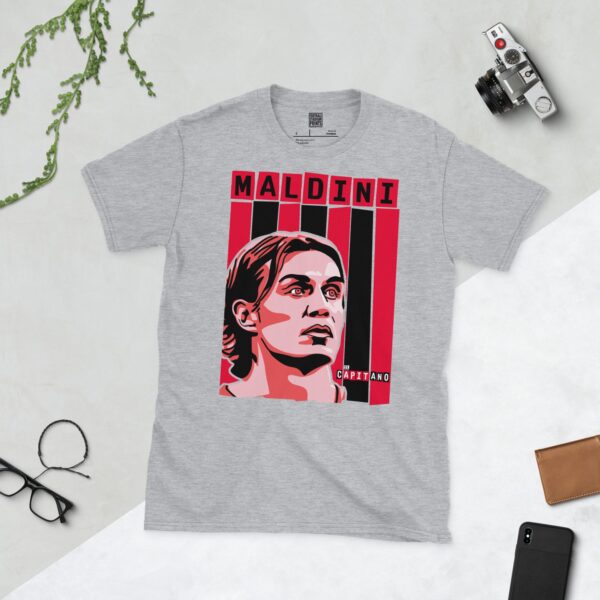 A versatile sports grey T-shirt showcasing a dynamic illustration of Paolo Maldini, the beloved AC Milan defender. The design includes his portrait over a vibrant red and black striped pattern, typical of the club's colours, with "MALDINI" and "IL CAPITANO" completing the tribute.