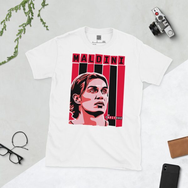 A crisp white T-shirt featuring a stylized graphic of AC Milan legend Paolo Maldini's face, positioned against bold red and black vertical stripes. His surname "MALDINI" is in block letters above, with "IL CAPITANO" subtly placed near his shoulder.