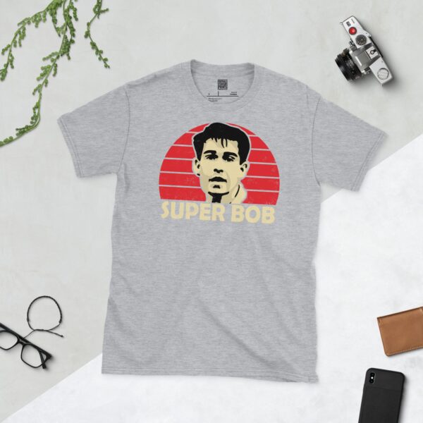 A versatile sports grey T-shirt showcasing a dynamic illustration of Bob Taylor, the beloved Bristol City striker. The design includes his portrait over a bold red radiating pattern, with "SUPER BOB" clearly visible underneath, celebrating the fan favourite.