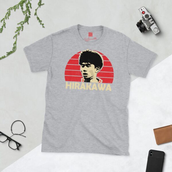 A versatile sports grey T-shirt showcasing a dynamic illustration of Yu Hirakawa, the memorable Bristol City midfielder. The design includes his portrait over a bold red radiating pattern, with "HIRAKAWA" clearly visible underneath.