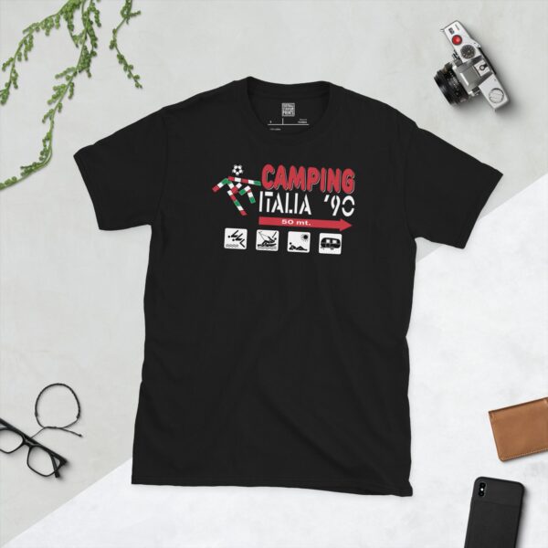 A bold black T-shirt emblazoned with a vivid "Camping Italia '90" graphic. The design prominently displays the event name, a football icon, and detailed camping pictograms (tent, boat, sunbather, caravan) with directional text, all set to evoke the spirit of the 1990 World Cup.