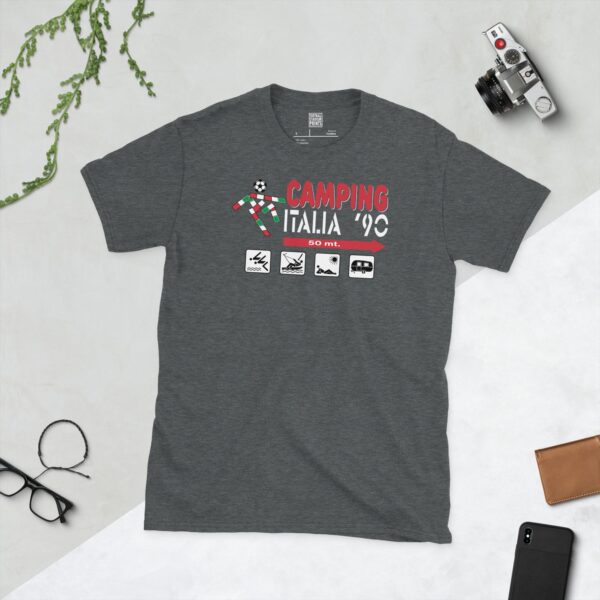 A subtle dark heather T-shirt displaying a distinctive "Camping Italia '90" graphic. The design comprises the event title, a football motif, and illustrative camping icons (tent, boat, sunbather, caravan) with a directional arrow and "50 mt.", offering a nostalgic nod to the 1990 World Cup.