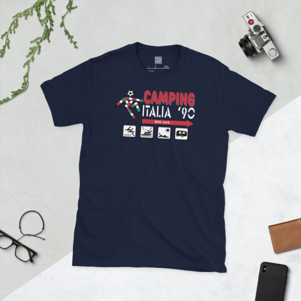 A deep navy blue T-shirt featuring a compelling graphic inspired by an old "Camping Italia '90" sign. The design includes the event title, a football icon in Italian flag colours, and a series of camping-related symbols with an arrow and distance, capturing retro football travel.