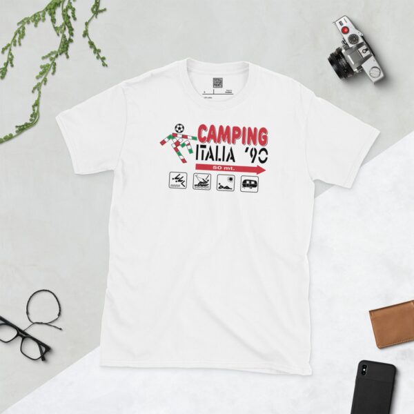 A clean white T-shirt featuring a retro graphic inspired by an Italia '90 camping sign. The design includes "CAMPING ITALIA '90", a football icon, and four small pictograms (tent, boat, sunbather, caravan) with an arrow and "50 mt.", all set against a subtle green and red background mimicking the Italian flag.