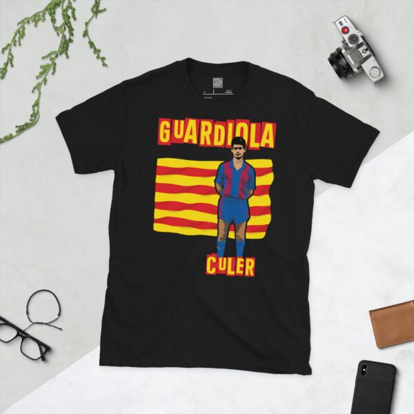 A bold black T-shirt emblazoned with a striking portrait of a young Pep Guardiola in his first Barcelona kit. The graphic depicts him against a backdrop of the Catalan flag, and the word "CULER" is a central feature below the image.