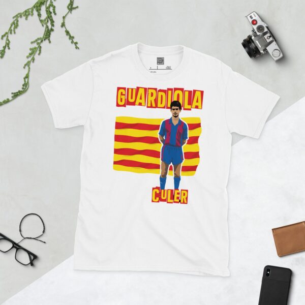 A clean white T-shirt featuring a stylized graphic of a young Pep Guardiola in his early Barcelona kit, set against a background of the red and yellow Catalan flag. The word "CULER" is prominently displayed below the portrait, celebrating his roots as a fan.