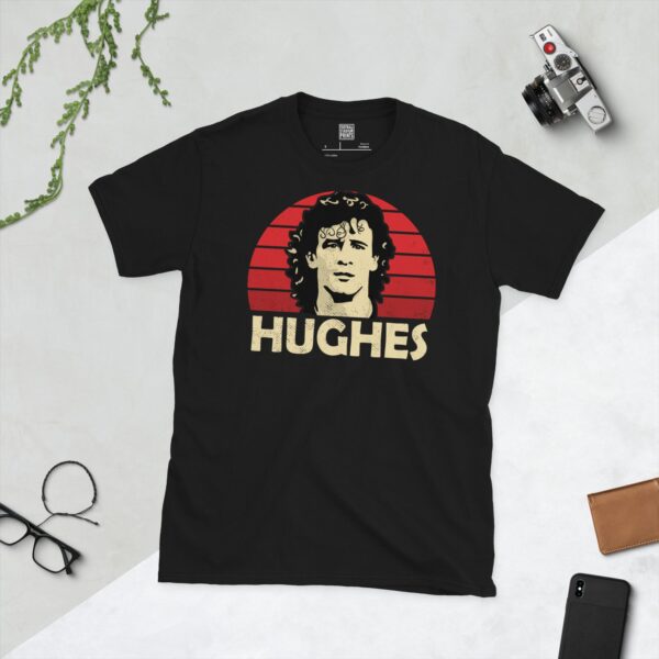 A bold black T-shirt emblazoned with a striking portrait of football icon Mark Hughes. The graphic depicts his face against a backdrop of red sunburst lines, and his surname "HUGHES" is a central feature below the image.