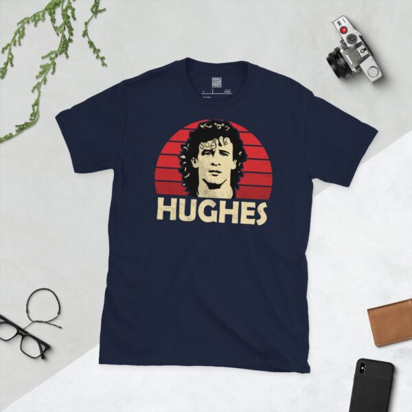A deep navy blue T-shirt featuring a compelling graphic of Mark Hughes, the legendary forward, with his image set against a vivid red sunburst design. His iconic surname "HUGHES" is clearly visible, paying tribute to his influential career.