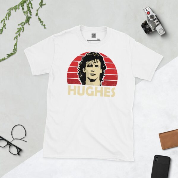A clean white T-shirt featuring a stylized graphic of football legend Mark Hughes's face, set against a vibrant red sunburst background, with his surname "HUGHES" prominently displayed below the portrait.
