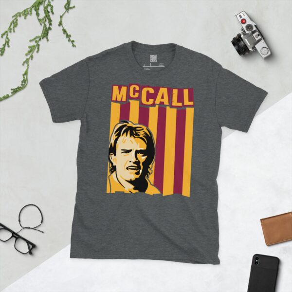A subtle dark heather T-shirt displaying a distinctive graphic of former Bradford City maestro Stuart McCall. His portrait is captured against a retro claret and amber striped backdrop, with his surname "MCCALL" directly above the illustration.