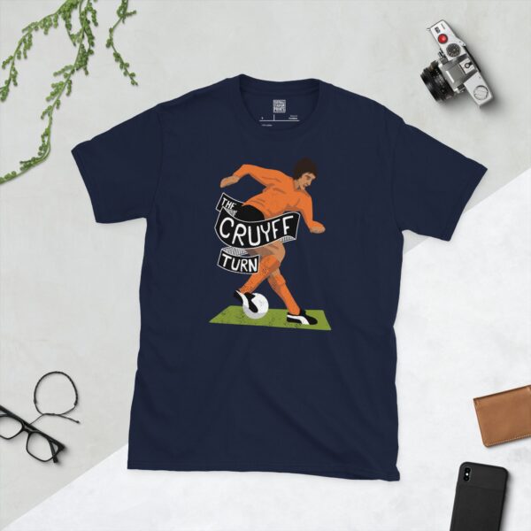 A deep navy blue T-shirt featuring a compelling graphic of Johan Cruyff, the legendary Dutch footballer. The design captures him performing his signature 'Cruyff Turn' with the words "THE CRUYFF TURN" alongside, honouring his influential move.