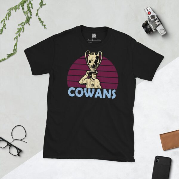 A bold black T-shirt emblazoned with a striking portrait of Aston Villa icon Gordon Cowans. The graphic depicts him lifting the European Cup against a backdrop of claret sunburst lines, and his surname "COWANS" is a central feature below the image.