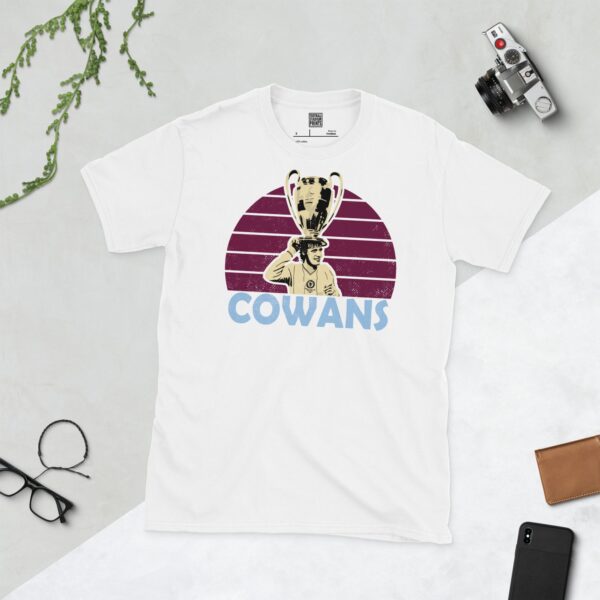 A clean white T-shirt featuring a stylised graphic of Aston Villa legend Gordon Cowans, holding the European Cup trophy, set against a vibrant sunburst background in a claret colour. His surname "COWANS" is prominently displayed below the portrait.