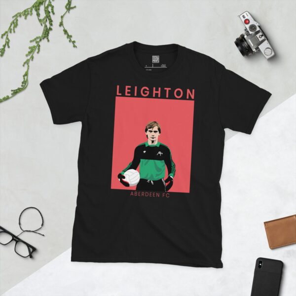 A black T-shirt featuring a stylised graphic of Aberdeen legend Jim Leighton in a goalkeeper kit. The surname "LEIGHTON" is printed above the image and "ABERDEEN FC" is printed below it, all set against a faded red background.