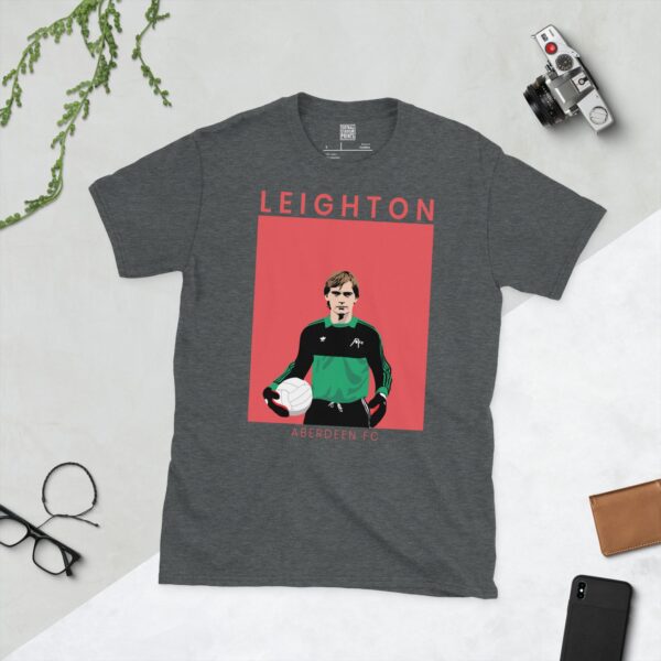 A subtle dark heather T-shirt displaying a distinctive graphic of former Aberdeen goalkeeper Jim Leighton. "LEIGHTON" is printed above his portrait, "ABERDEEN FC" is printed below, and the image is captured against a retro faded pink background.