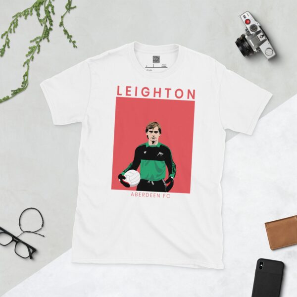 A clean white T-shirt emblazoned with a striking portrait of Aberdeen icon Jim Leighton. The graphic is flanked by "LEIGHTON" above and "ABERDEEN FC" below, with a backdrop of faded red.