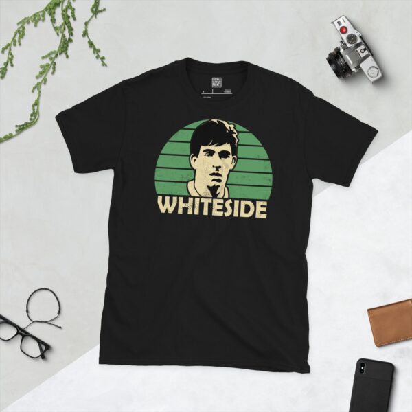 A bold black T-shirt emblazoned with a striking portrait of Northern Ireland icon Norman Whiteside. The graphic depicts his face against a backdrop of green sunburst lines, and his surname "WHITESIDE" is a central feature below the image.