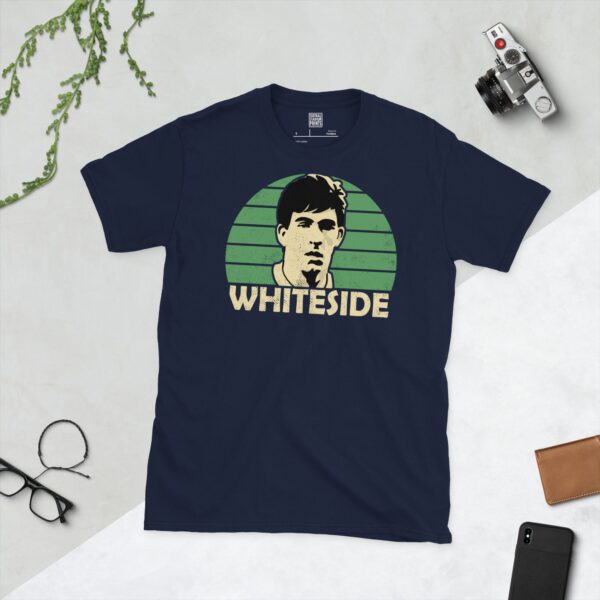 A deep navy blue T-shirt featuring a compelling graphic of Norman Whiteside, the legendary Northern Ireland player, with his image set against a vivid green sunburst design. His iconic surname "WHITESIDE" is clearly visible, paying tribute to his time with the national team.