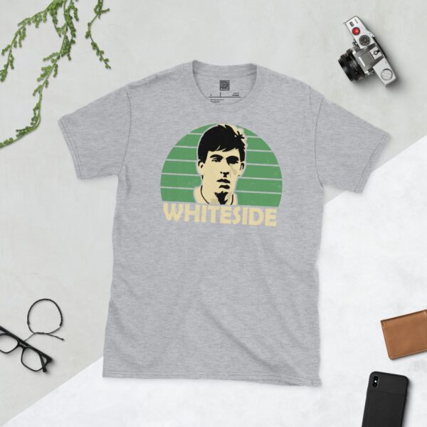 A versatile sports grey T-shirt showcasing a dynamic illustration of Norman Whiteside, the beloved Northern Ireland forward. The design includes his portrait over a bold green radiating pattern, with "WHITESIDE" clearly visible underneath.