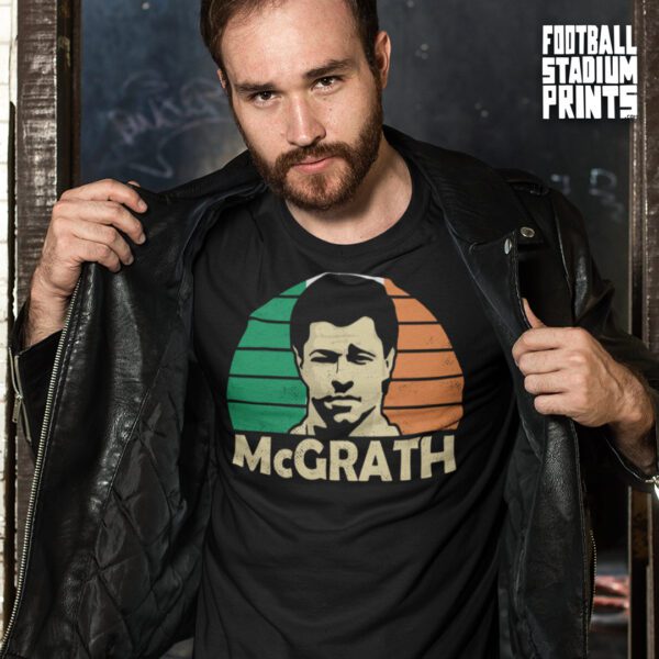 A man wearing a leather jacket and opening it up to reveal a black t-shirt featuring Irish football legend Paul McGrath