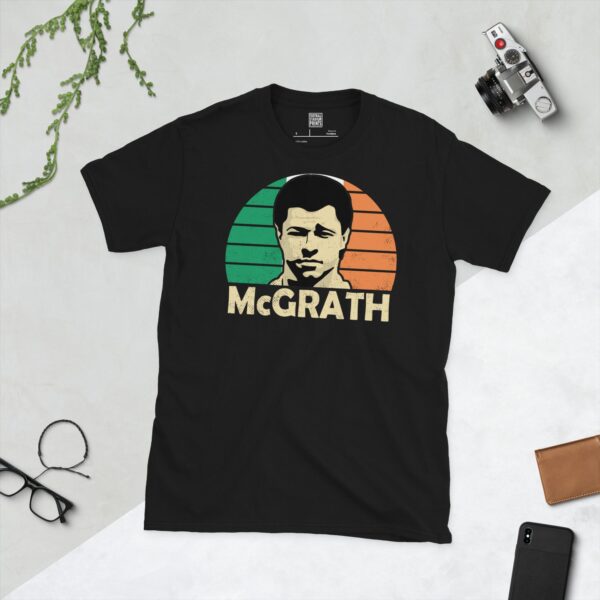 A bold black T-shirt emblazoned with a striking portrait of Republic of Ireland icon Paul McGrath. The graphic depicts his face against a backdrop of green, white, and orange sunburst lines, and his surname "MCGRATH" is a central feature below the image.