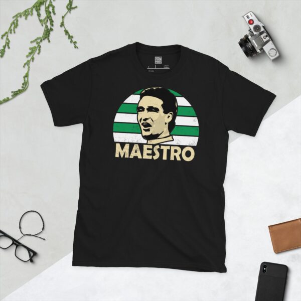 A bold black T-shirt emblazoned with a striking portrait of Celtic icon Paul McStay. The graphic depicts his face against a backdrop of green and white striped sunburst lines, and his famous nickname "MAESTRO" is a central feature below the image.