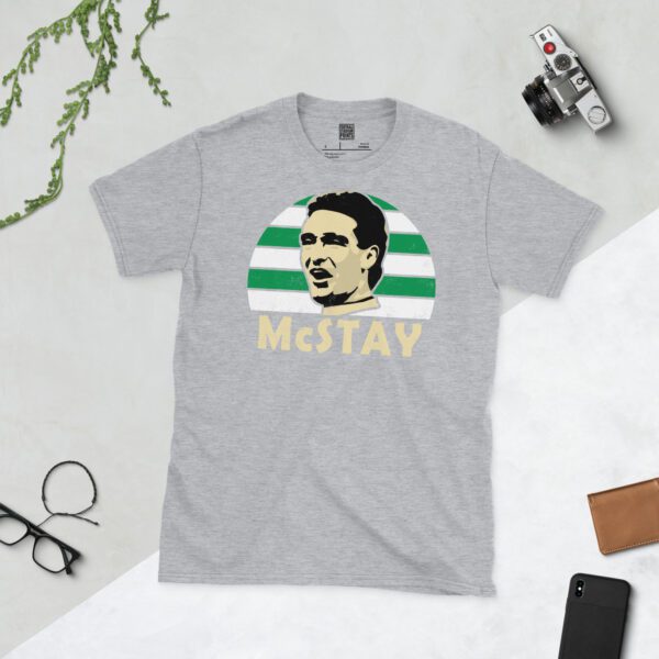 A versatile sports grey T-shirt showcasing a dynamic illustration of Paul McStay, the beloved Celtic midfielder. The design includes his portrait over a bold green and white striped radiating pattern, with "McSTAY" clearly visible underneath.