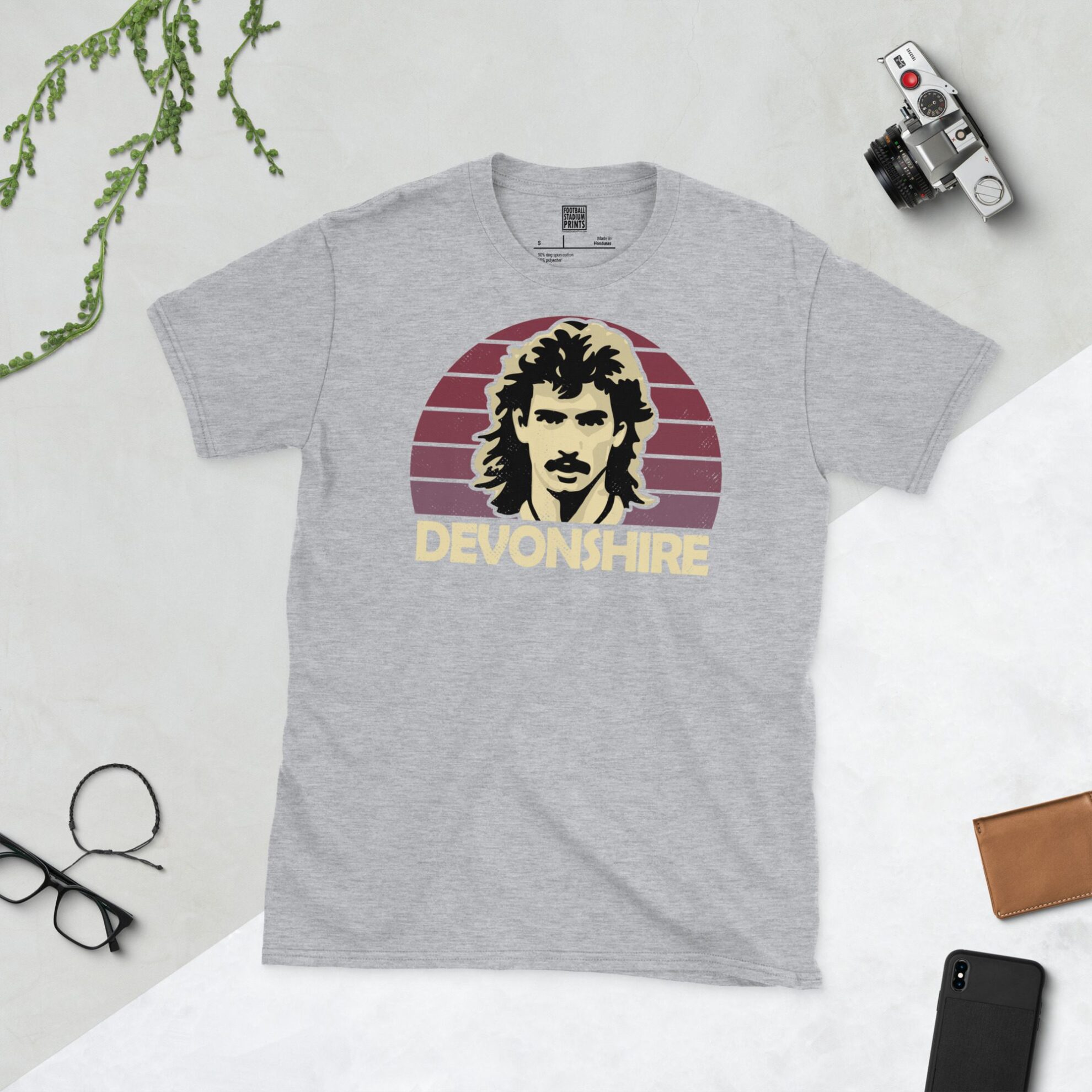 A sports grey T-shirt featuring a unique graphic of West Ham's Alan Devonshire. The image is backed by a claret sunburst and the text "DEVONSHIRE" is printed in light yellow below the portrait.