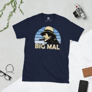 A navy T-shirt displaying an artistic illustration of Malcolm Allison, the former Man City manager. The graphic is backed by a light blue faded sunburst and the nickname "BIG MAL" appears underneath in light yellow.