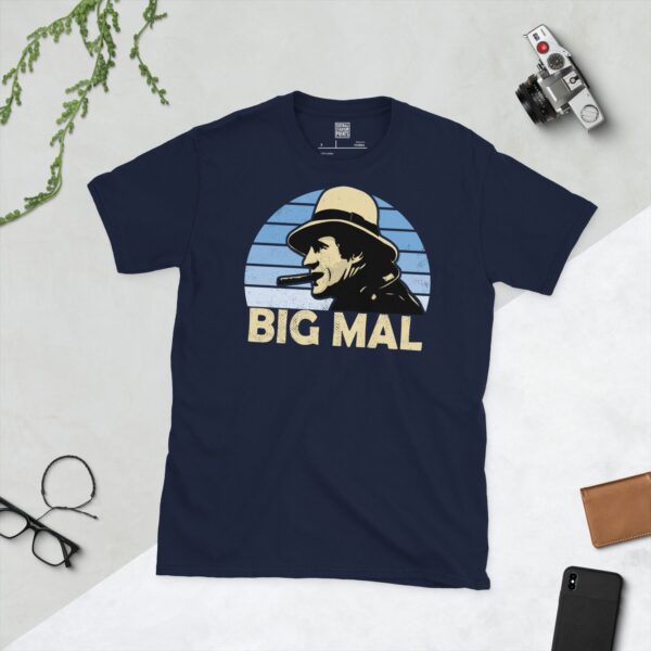 A navy T-shirt displaying an artistic illustration of Malcolm Allison, the former Man City manager. The graphic is backed by a light blue faded sunburst and the nickname "BIG MAL" appears underneath in light yellow.