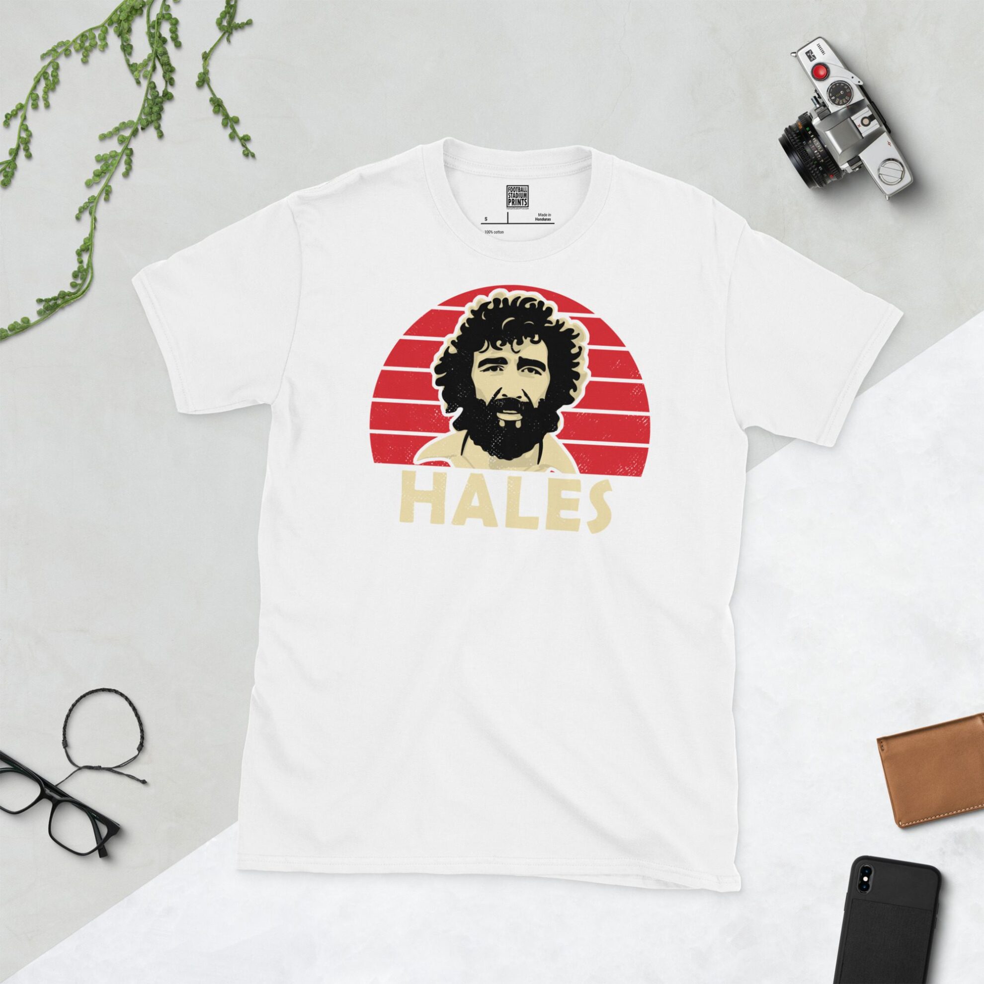 A white T-shirt with a bold portrait of football legend Derek Hales. The image is set against a red sunburst background with the name "HALES" in light yellow underneath.
