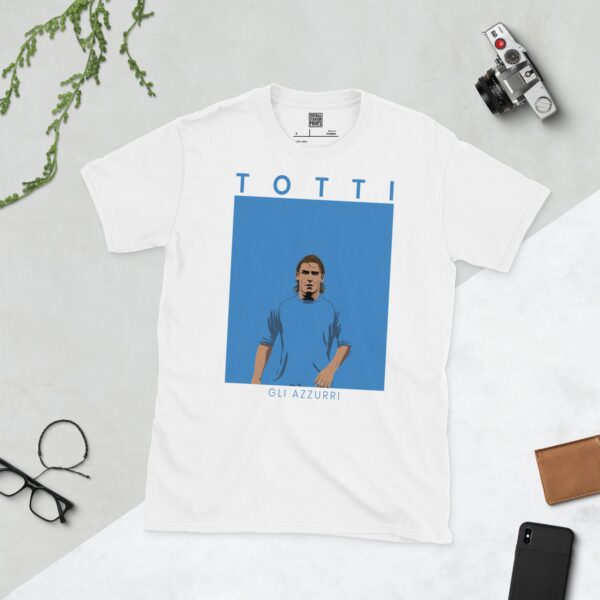 A white T-shirt with a contemporary graphic of Francesco Totti in a light blue top, with the text "TOTTI" above and "GLI AZZURRI" below the image.