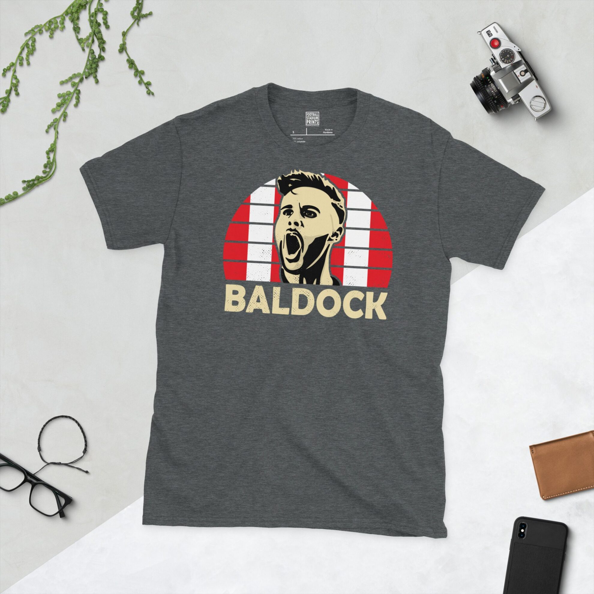 A dark heather T-shirt showing a clean, modern portrait of George Baldock, the Blades icon, with "BALDOCK" printed in white below the image on a red and white checkered background.