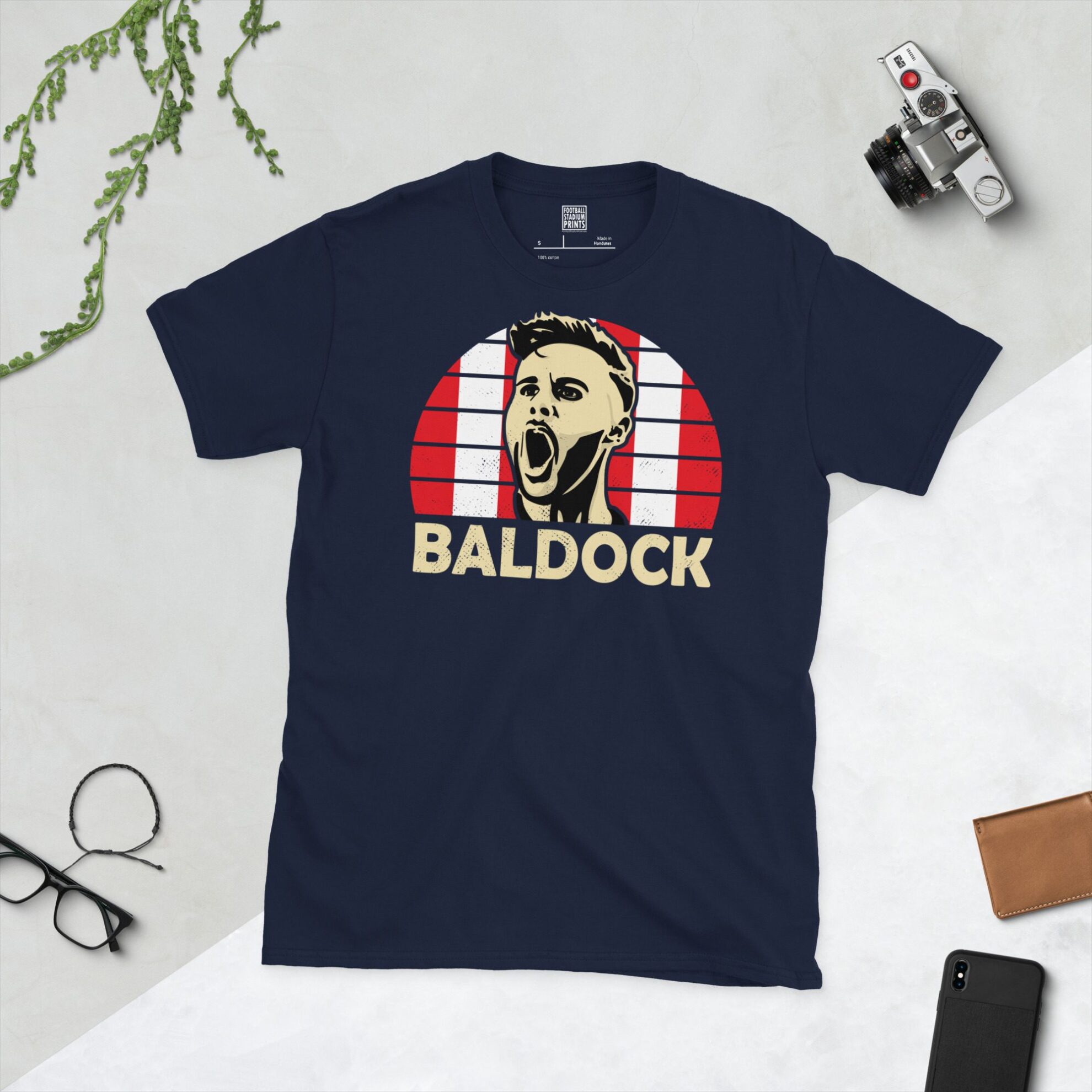A navy T-shirt displaying an artistic illustration of George Baldock, the popular Sheffield United defender. The graphic is backed by a red and white checkered sunburst and the name "BALDOCK" appears underneath in white.